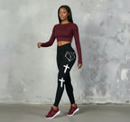 Woman wearing a black athletic outfit with designs against a gray concrete wall.